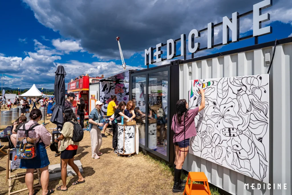 Pop-up zóna fashion brandu Medicine na festivale Pohoda s veľkým nápisom MEDICINE a plátnom na vyfarbovanie na presklenej kontajnerovej stavbe